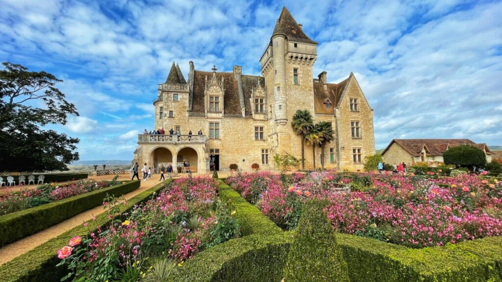 Vue de face château des Milandes en Dordogne avec ciel dégagé et parterre de fleurs